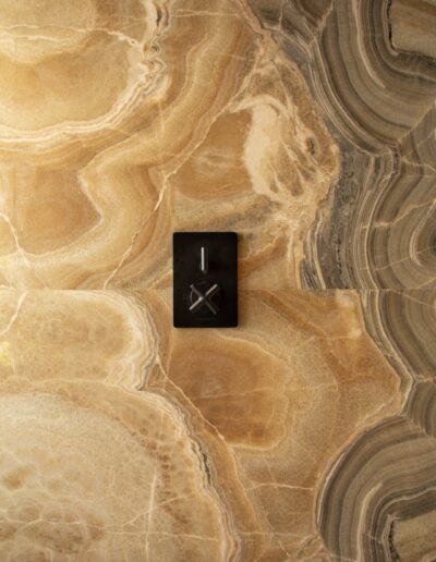 A black switch panel with a lever and dial is mounted on a polished, beige and gray marble wall with swirling patterns.